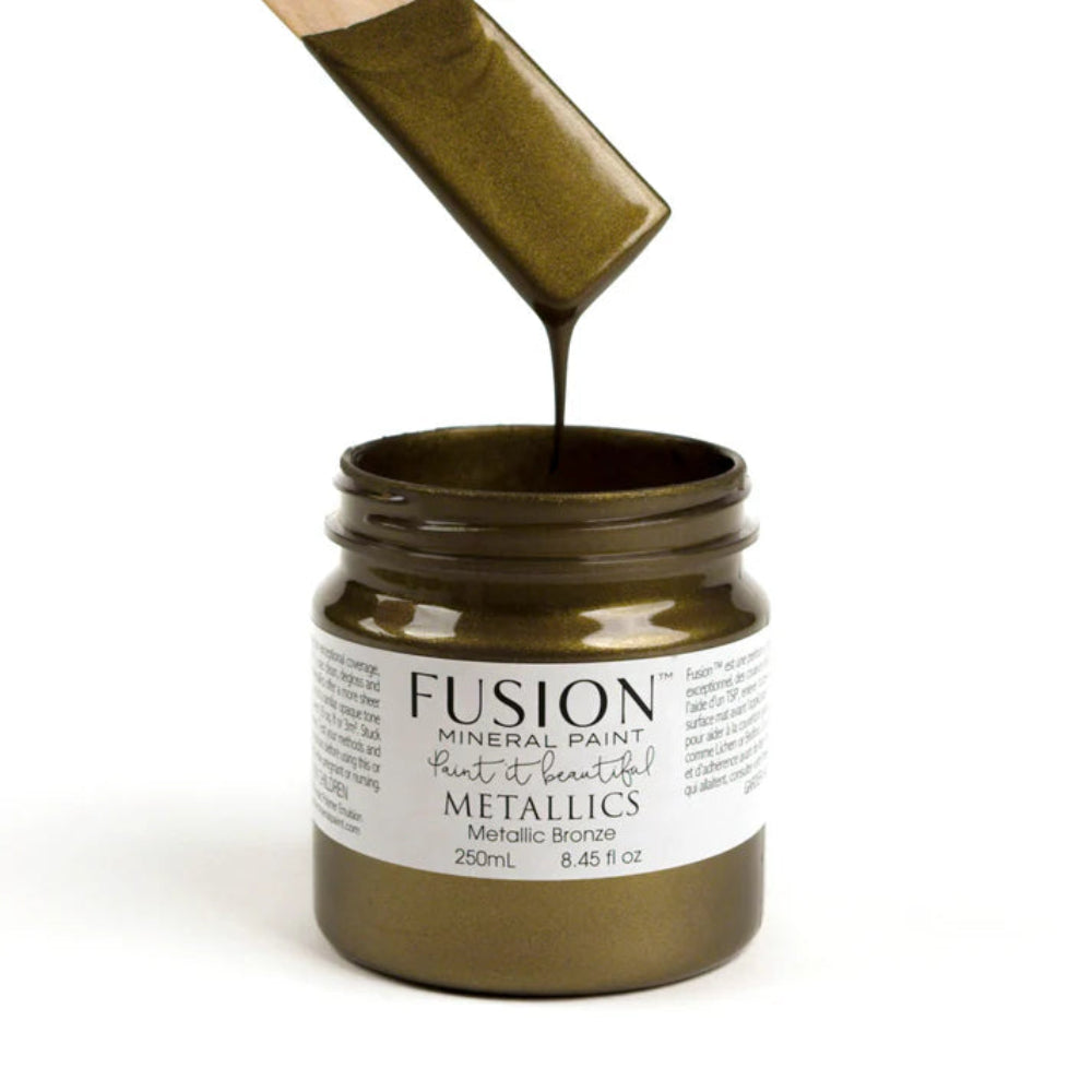 Jar of Fusion Mineral Paint Metallics in Bronze with a brush pouring paint