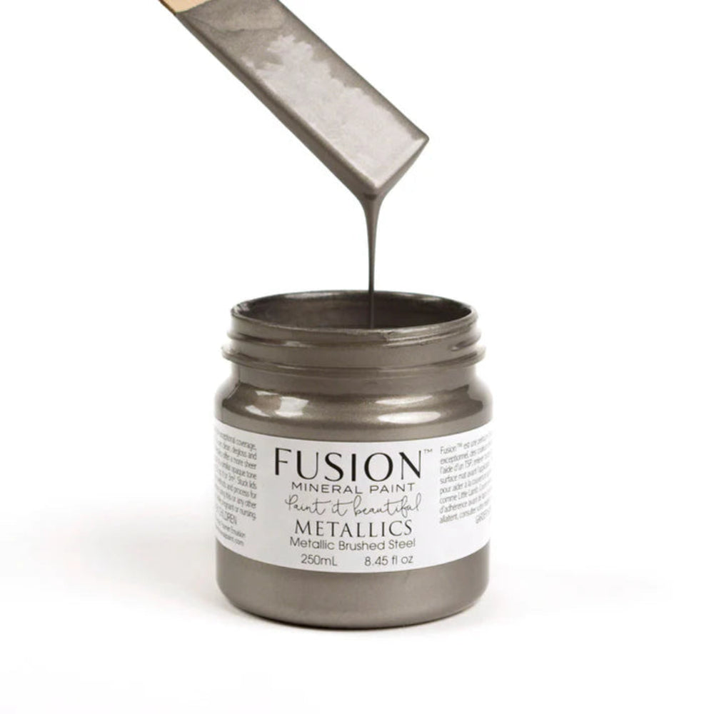 Jar of Fusion Mineral Paint Metallics in Brushed Steel with a paintbrush dipping into the paint