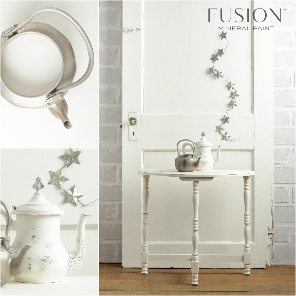 An old door painted in Fusion Casement white paint with a decorative table, teapots and star-shaped ornaments against a white wall.