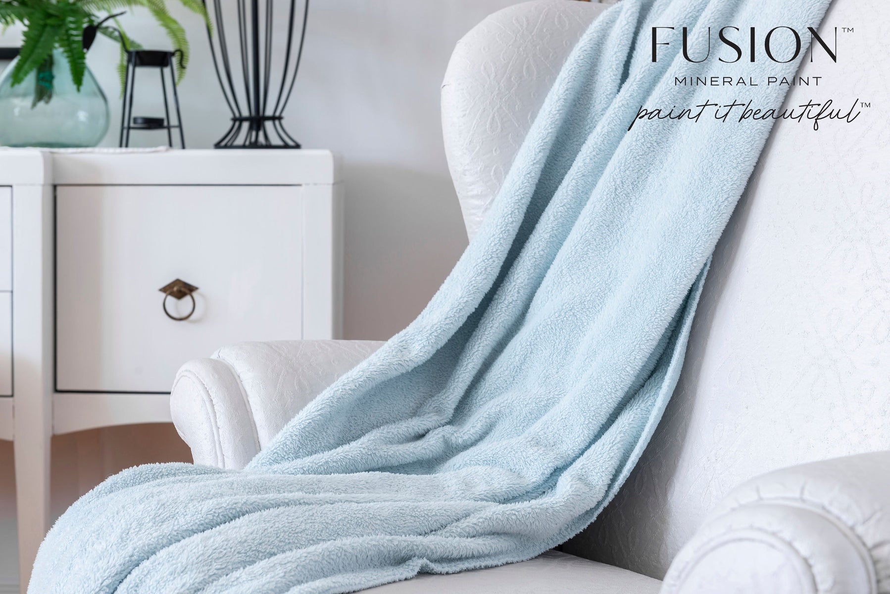 Light blue blanket draped over a white armchair with Fusion Mineral Paint branding.