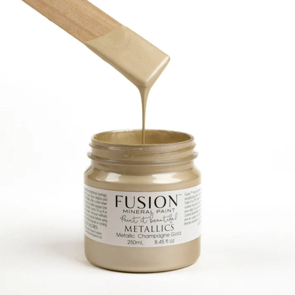 Jar of Fusion Mineral Paint in Metallic Champagne Gold with a wooden stirrer, on a white background