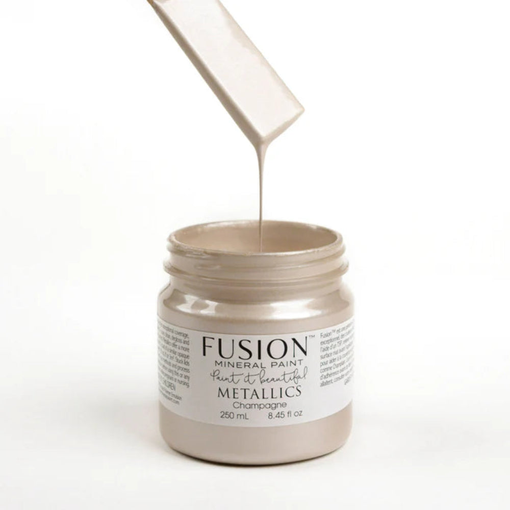 Jar of Fusion Mineral Paint in Metallic Champagne with paint being poured into it on a white background