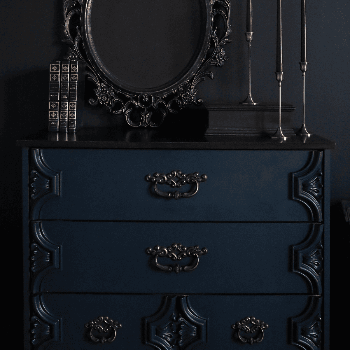 Dresser painted in Fusion Mineral Paint Chestler, a dark green blue, with a decorative mirror, books and candles against a black background.