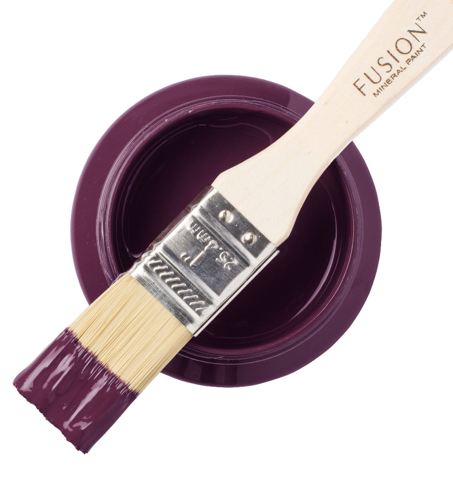 Paintbrush dipped in brilliantly purple Elderberry Fusion Mineral Paint laid across a paint container against a white background