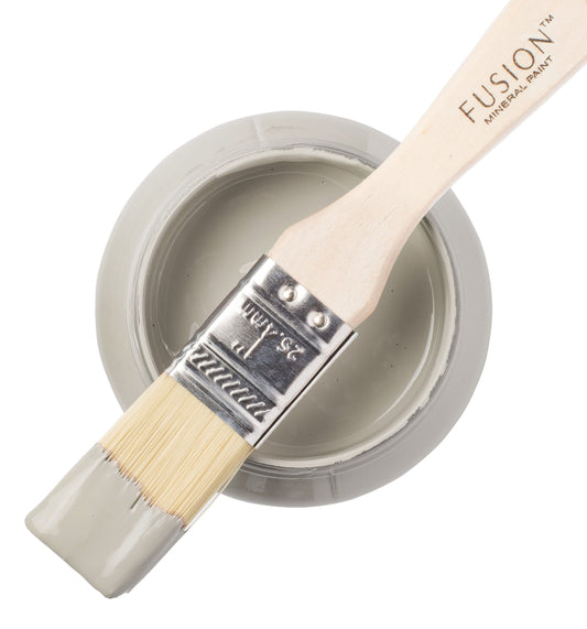 A paintbrush dipped in Eucalyptus shade of Fusion Mineral Paint rested on top of a tin of paint