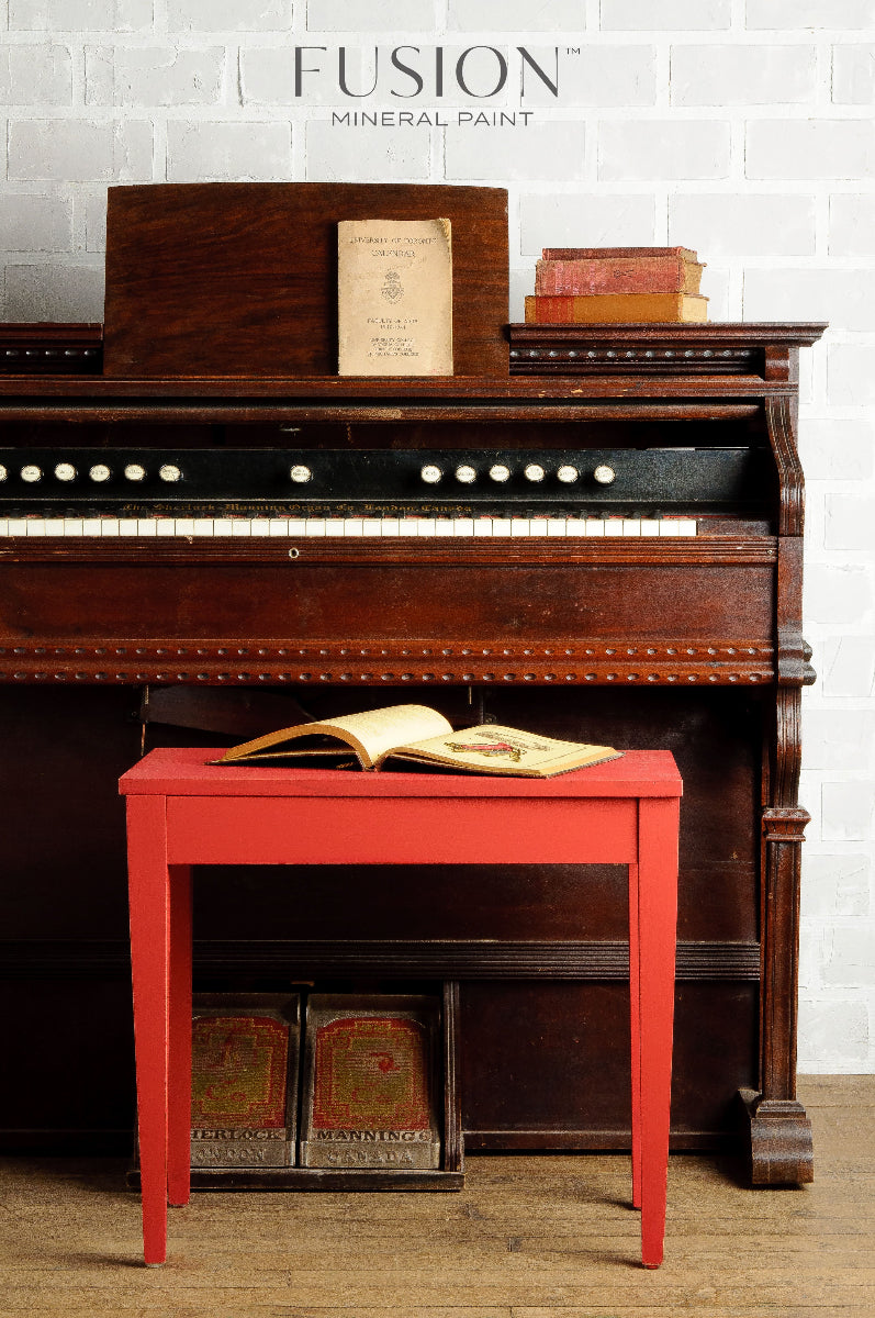 Vintage piano with a Fort York Red painted stool against a white brick wall, featuring Fusion Mineral Paint branding.
