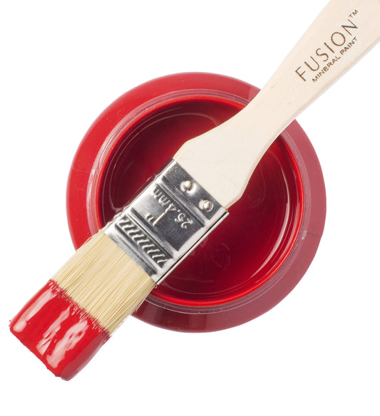 A paintbrush dipped in Fort York Red Fusion Mineral Paint resting on a tin of red paint