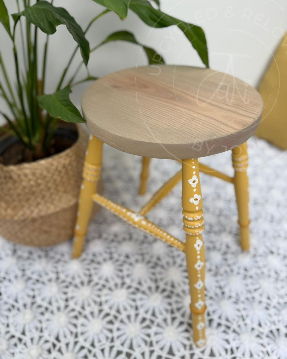 Upcycled stool with a raw pine top and legs painted in Fusion Mineral Paint in Prairie Sunset, a mustard yellow, finished with hand-painted folk-inspired decorative patterns in white.