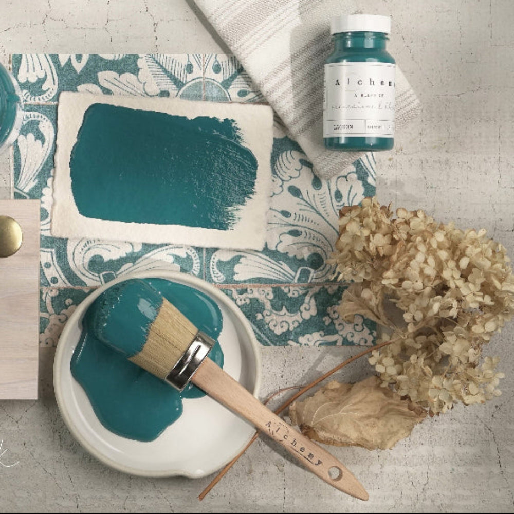 Blue-green Lagoon Alchemy paint with a brush, container, and decorative elements on a textured surface