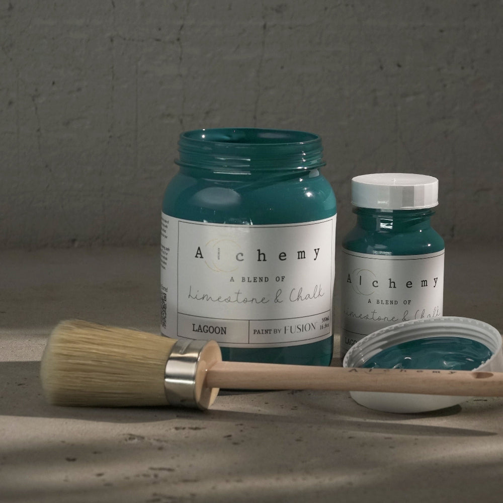 Two jars of greeny-blue Lagoon paint from Alchemy by Fusion with a brush on a textured surface