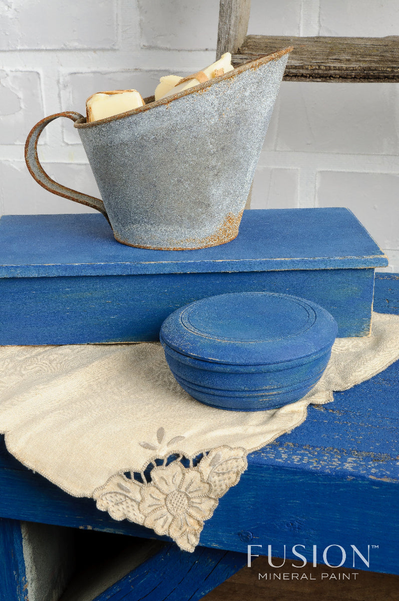 A table painted in Liberty Blue from the Fusion Mineral Paint range with a metal jug and linen tablecloth against a white wall