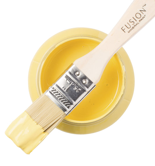 Paint brush with yellow Little Star paint from the Fusion Mineral Paint range laid across a container on a white background