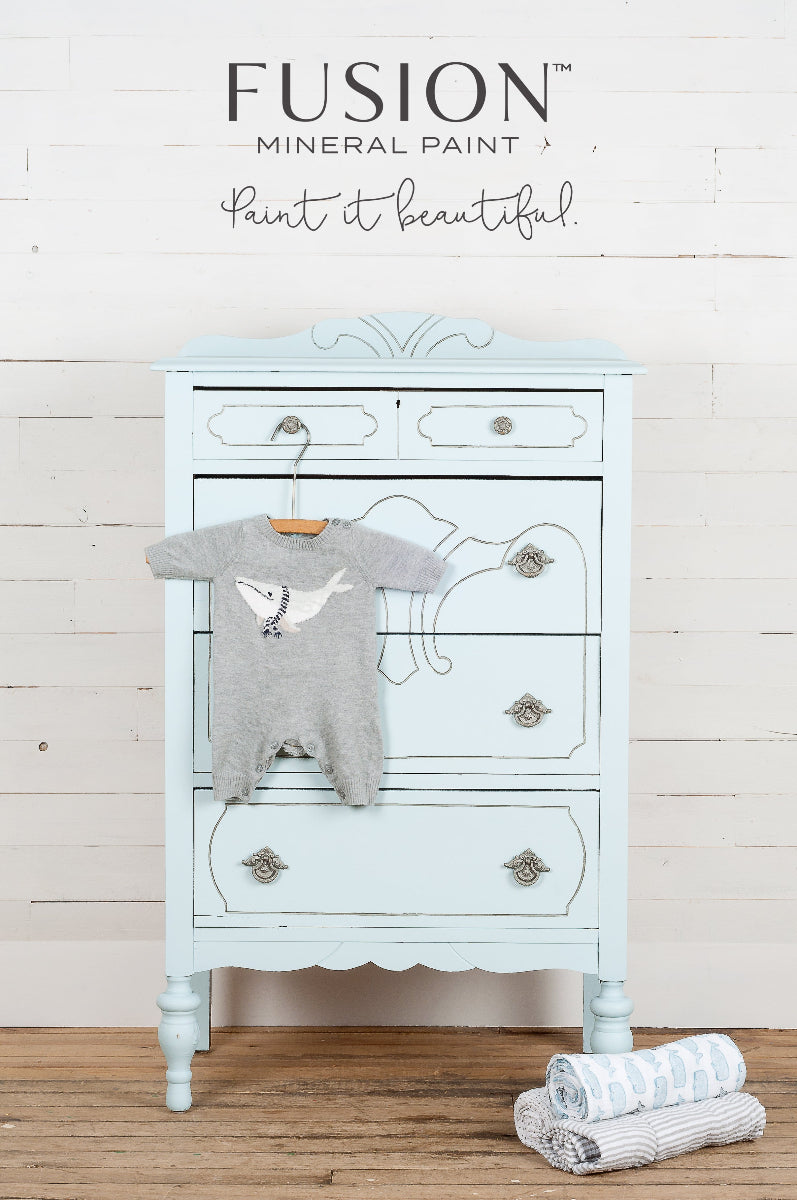 Light blue dresser painted in Little Whale from the Fusion Mineral Paint range, with a grey baby romper and white towels on a wooden floor
