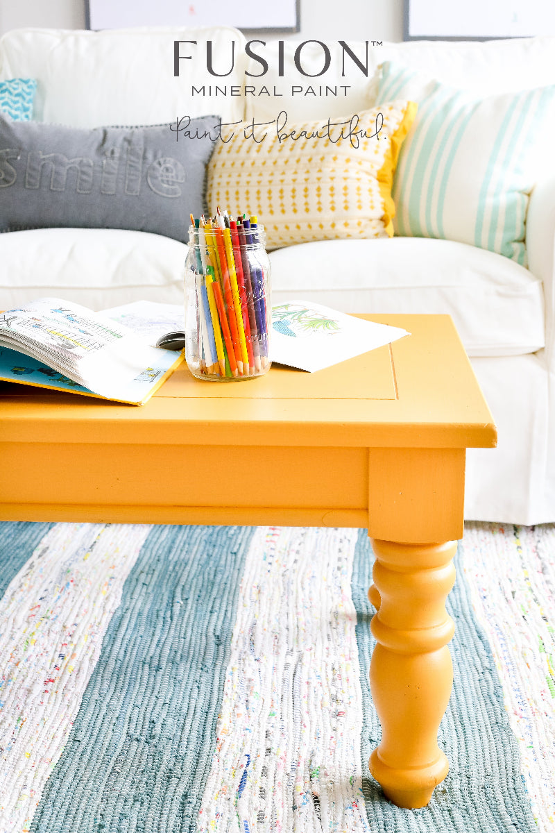 Mustard painted coffee table with colourful pencils and books in front of a white couch