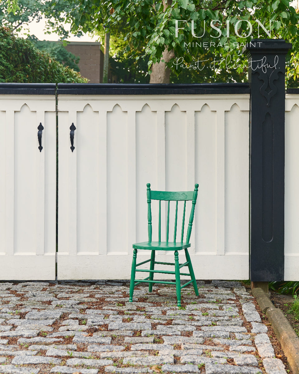 Wooden chair painted in gorgeous green Park Bench from Fusion Mineral Paint positioned in front of a white fence