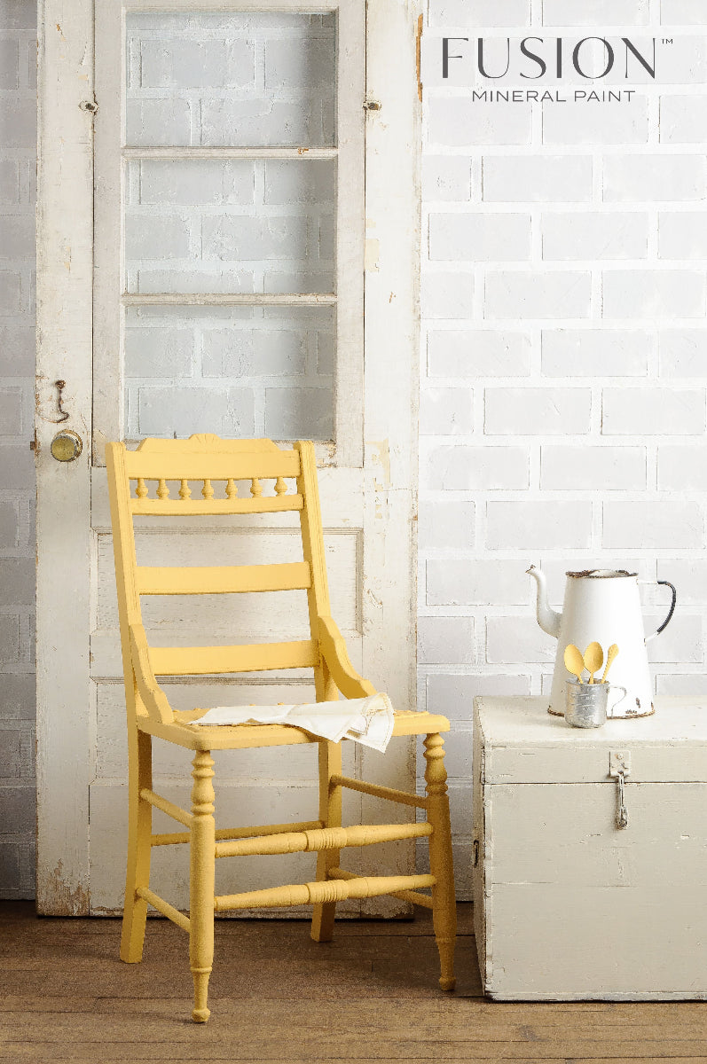 Wooden chair painted in beautiful yellow Prairie Sunset from the Fusion Mineral Paint range against a white brick background