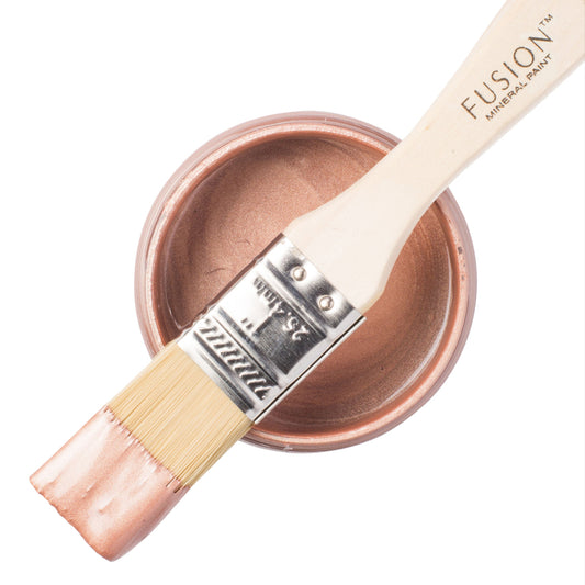 Rose Gold Metallic paint on a brush resting on top of an open paint jar  on a white background