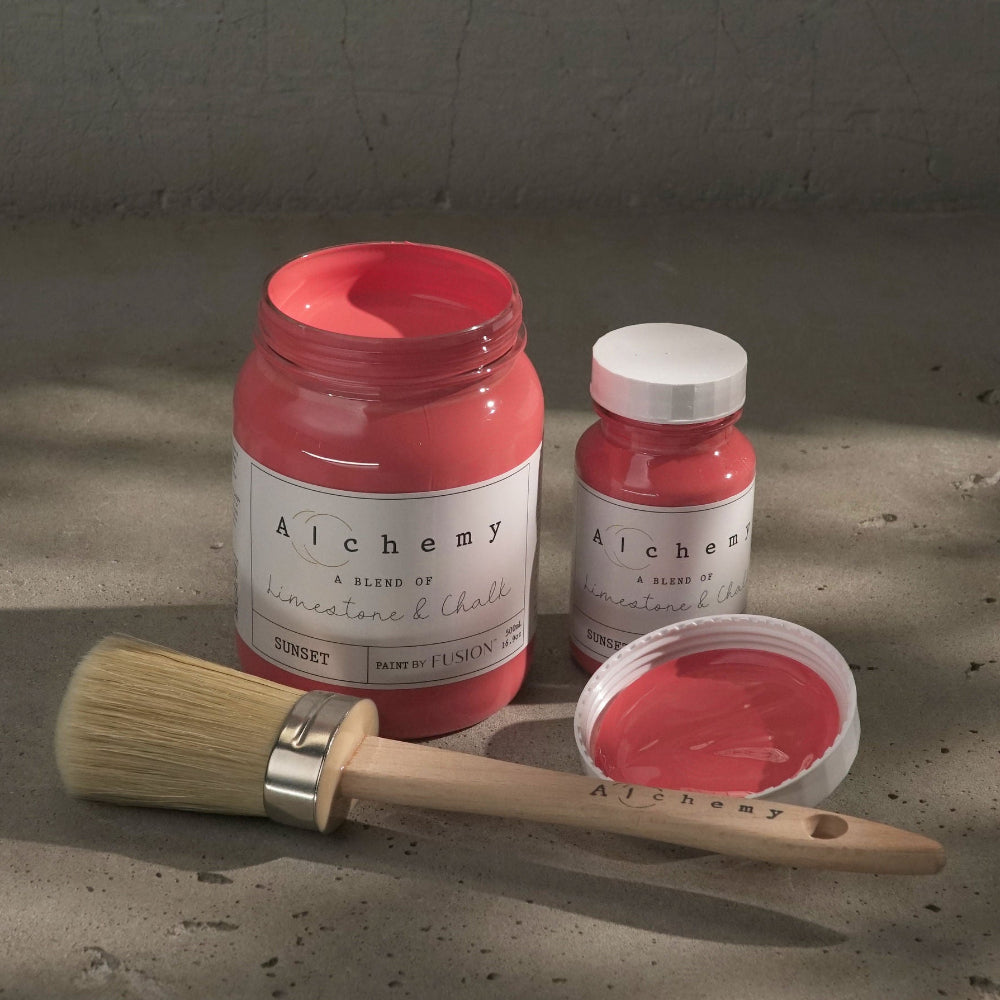 Jars of vibrant coral-coloured Sunset paint from Alchemy by Fusion against a plain textured background