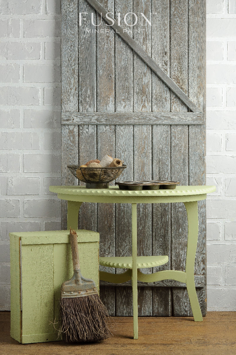 Table painted in Upper Canada Green from Fusion Mineral Paints with decorative items against a rustic wooden door and white brick wall.