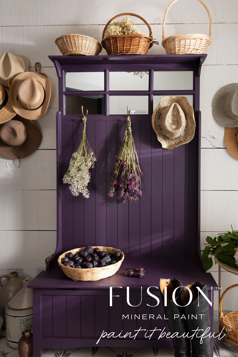 Storage bench painted in Velvet Plum from the Fusion Mineral Paint range with hats, baskets, and flowers against a white tiled wall