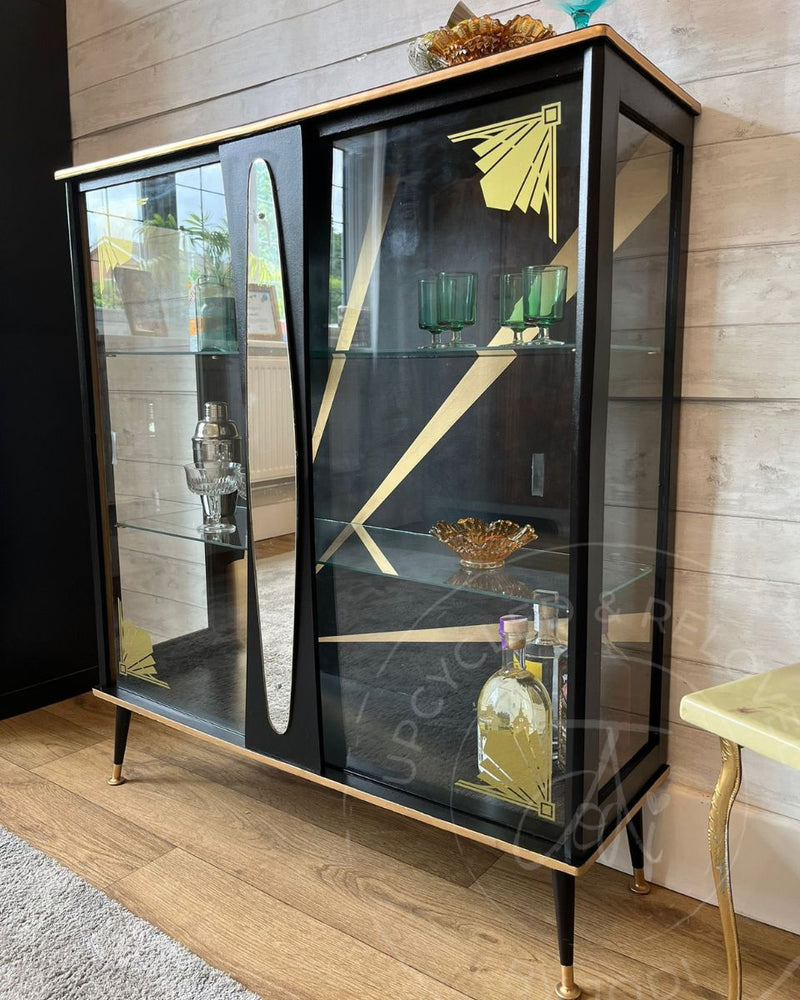 A black and gold vintage glass drinks cabinet with cleaned glass shelves, gold edging, sunburst detail and restored feet after a Marketplace furniture makeover from Upcycled & Reloved by Jodi. 