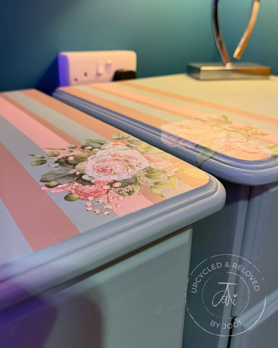 A pair of upcycled pine bedside cabinets, showing the tops, with a floral design and striped pattern in pink hues and a duck egg blue base.  