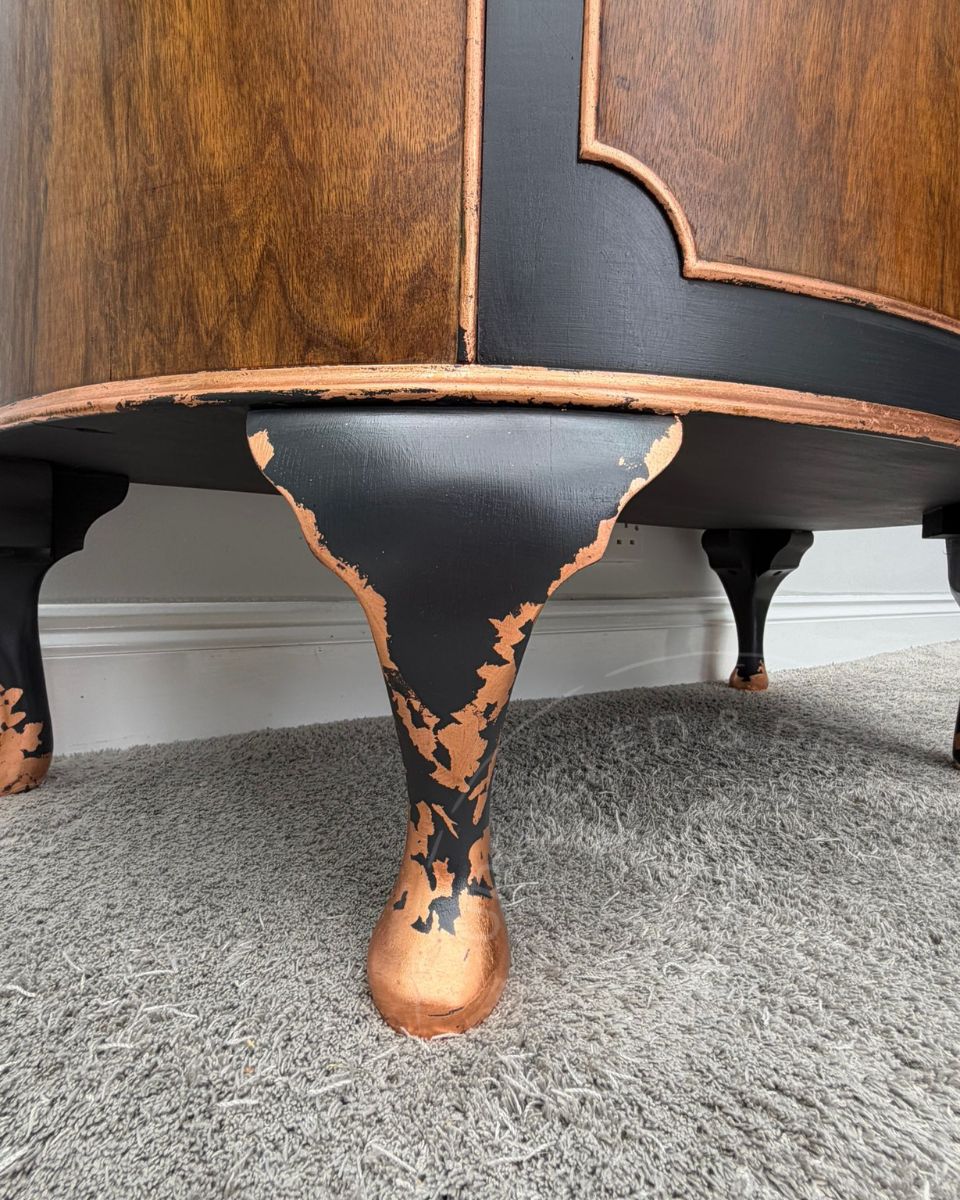 Close of Queen Anne feet on a demi lune cabinet that have been painted in Fusion Ash black and accented with copper leaf. 