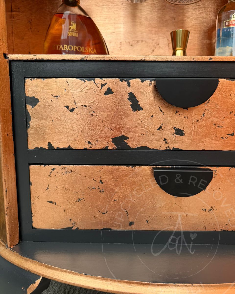 A close up of two draws inside a demi lune cabinet that have been painted in Fusion Mineral Paint Ash, a charcoal black, and finished in copper leaf to match the back of the inside cabinet. 