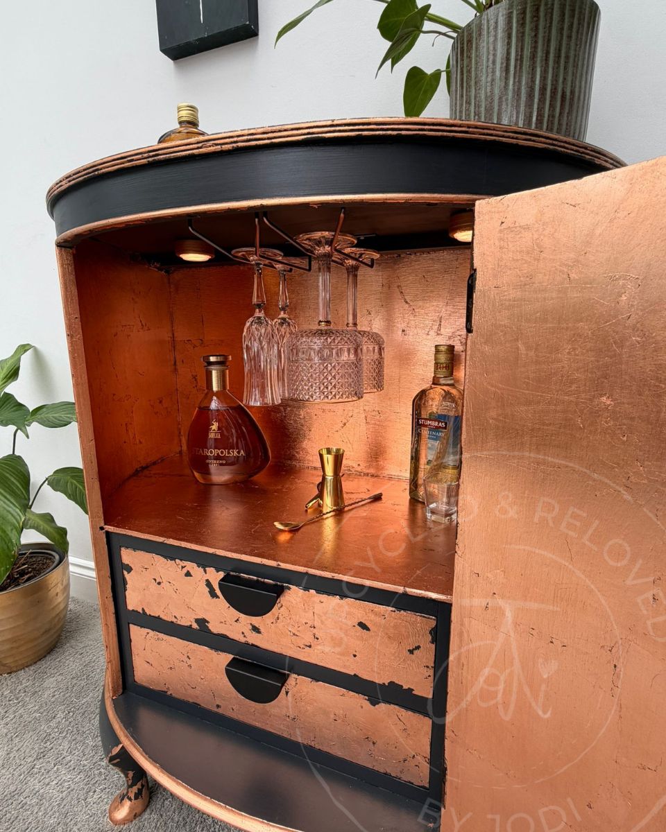 Upcycled bow fronted demi lune cabinet showing the inside with hanging glasses and a shimmering copper leaf finish across the shelves, back, drawers and inside of door. 