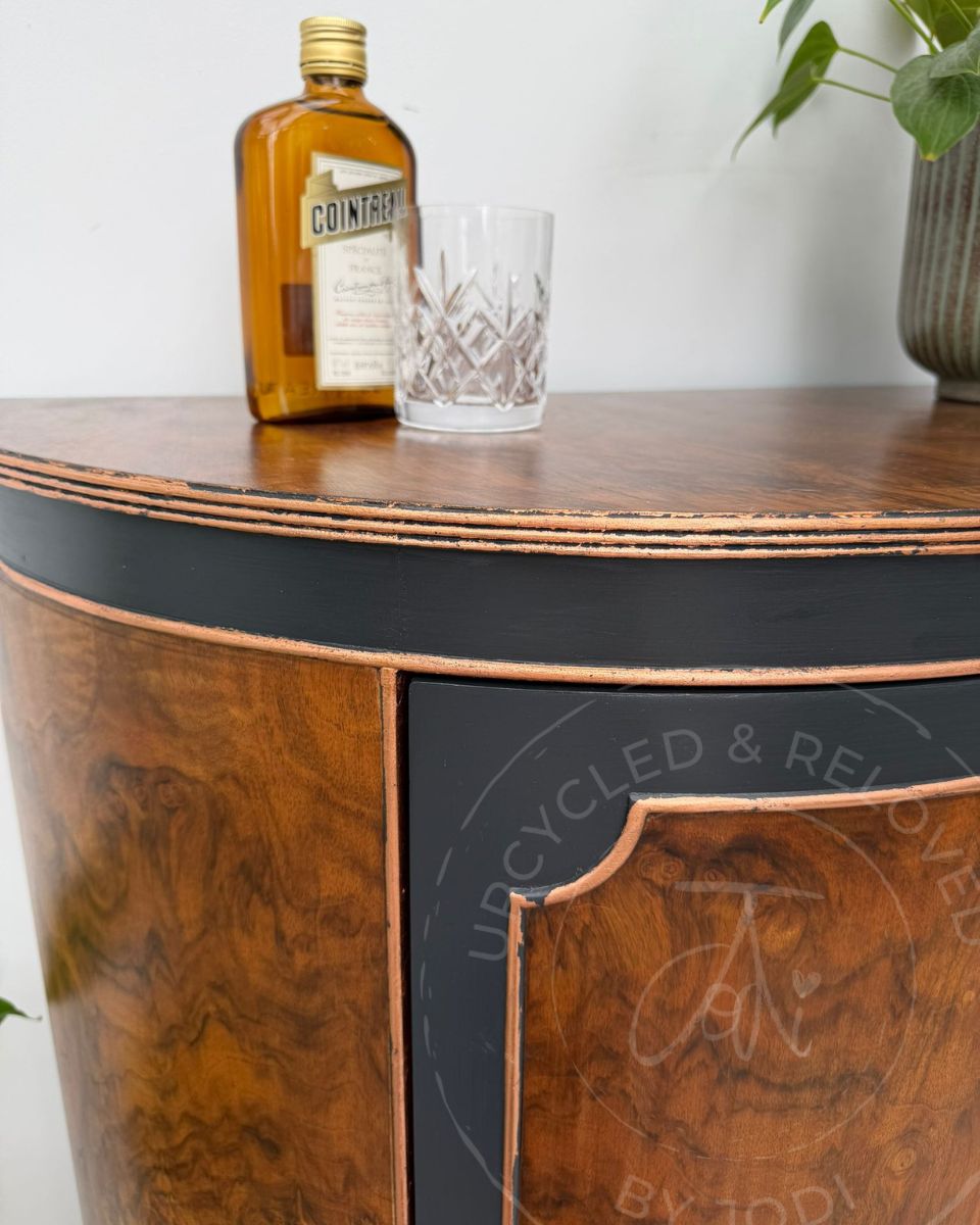 Upcycled demi-lune drinks cabinet in walnut, Fusion Ash black, and finished with copper leaf, showing a bottle of alcohol placed on top. 