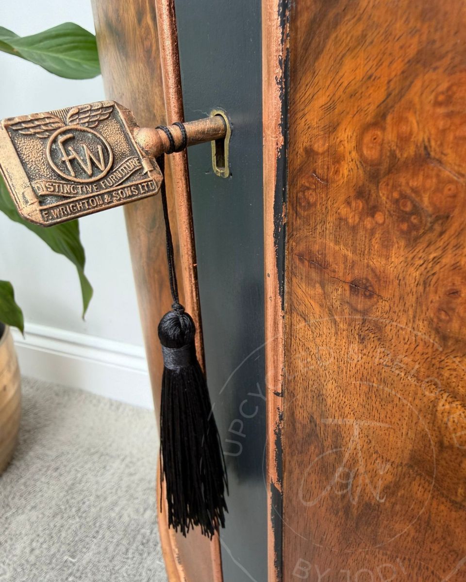 Close up of a copper-finished key decorated with a black tassel, hanging from an upcycled walnut, black and copper bow fronted demi-lune drinks cabinet. 