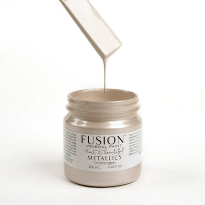 Jar of Fusion Mineral Paint in Metallic Champagne with paint being poured into it on a white background