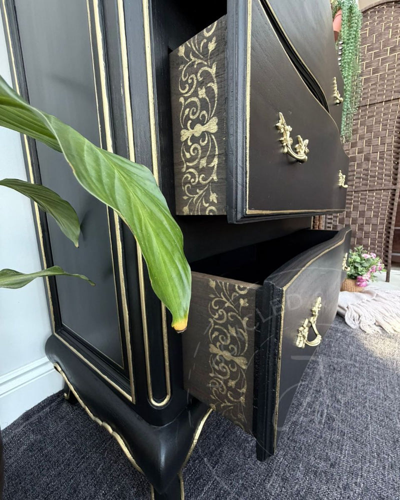 Black and gold chest of drawers with gilded gold handles and decorative edging, and stencilled drawer sides, refinished by Upcycled & Reloved by Jodi.