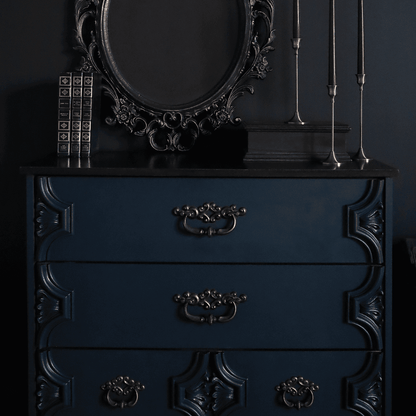 Dresser painted in Fusion Mineral Paint Chestler, a dark green blue, with a decorative mirror, books and candles against a black background.