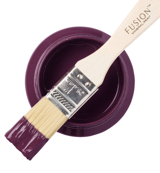 Paintbrush dipped in brilliantly purple Elderberry Fusion Mineral Paint laid across a paint container against a white background