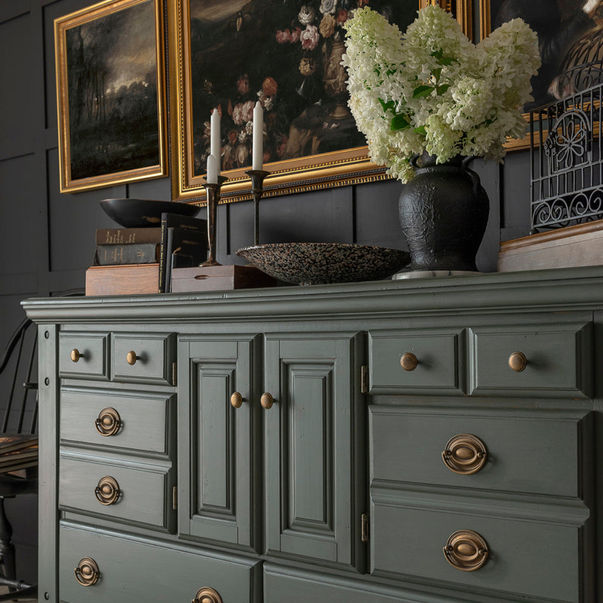 Dresser painted in Fusion Mineral Paint Everett, a weathered olive green, adorned with a vase, candlesticks and old books.