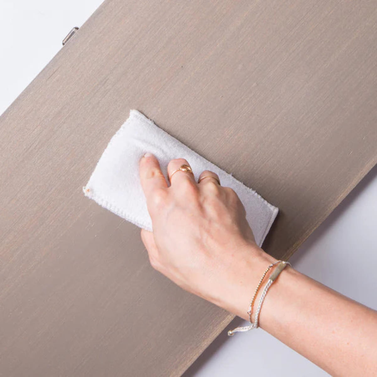 A woman's hand showing her using a  Fusion Mineral Paint Applicator Pad to apply a finish to a light-coloured wooden board