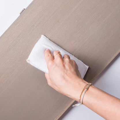 A woman's hand showing her using a  Fusion Mineral Paint Applicator Pad to apply a finish to a light-coloured wooden board