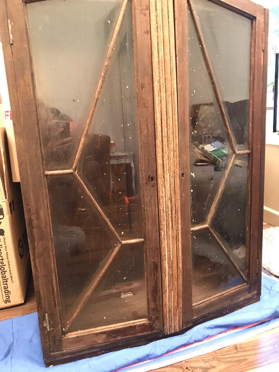A bare wood gin cabinet with glass pane doors and no legs in a worn condition prior to being upcycled. 