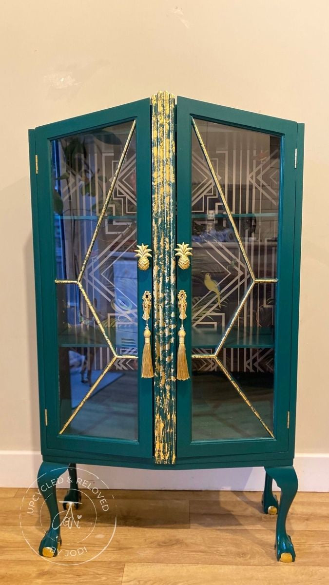 An upcycled gin cabinet with ball and claw feet, painted in a dark green with gold gilding finishes and gold pineapple door handles. 