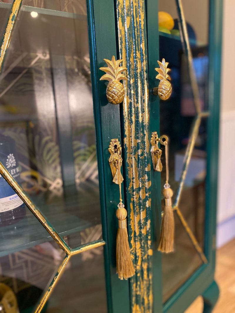 Decorative upcycled gin cabinet with glass doors, painted in green with gold pineapple and tassel details