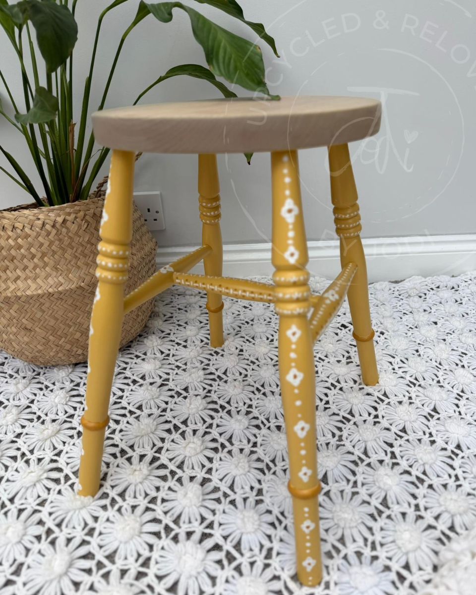 Upcycled stool with a raw pine top and legs painted in Fusion Mineral Paint in Prairie Sunset, a mustard yellow, finished with white hand-painted folk-inspired decorative patterns. 