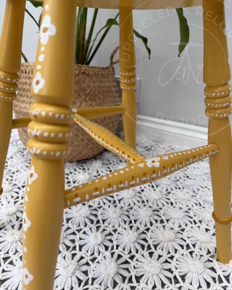 Close up of upcycled stool legs painted in Fusion Mineral Paint in Prairie Sunset, a mustard yellow, finished with hand-painted folk-inspired decorative patterns in white. 