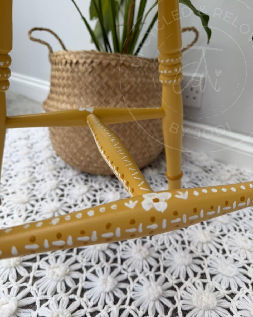 Close up of upcycled stool legs painted in Fusion Mineral Paint in Prairie Sunset, a mustard yellow, finished with hand-painted folk-inspired decorative patterns in white. 