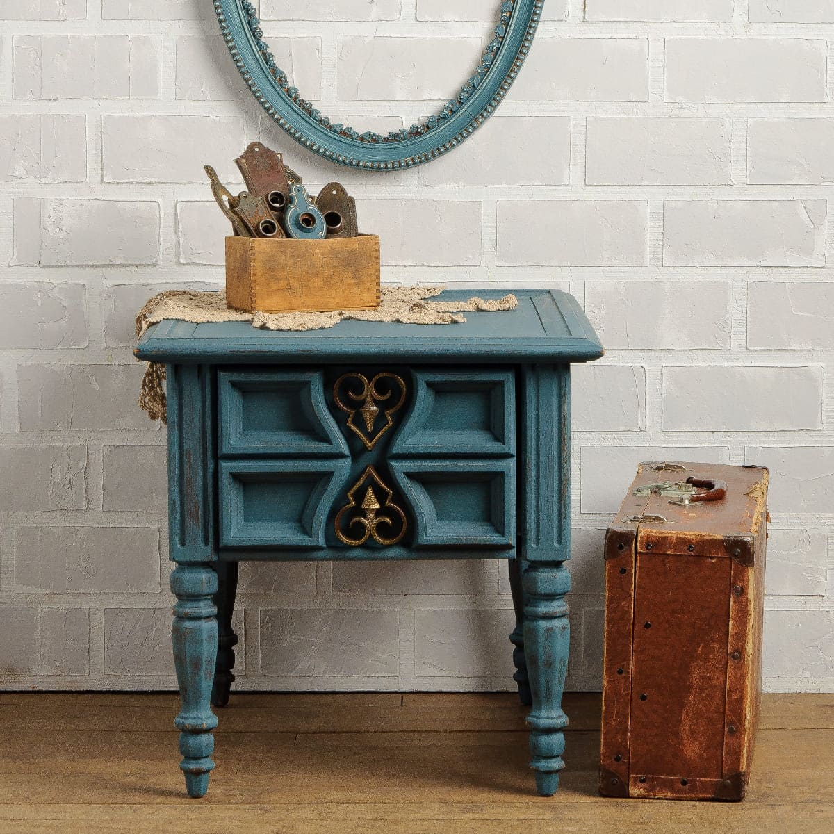 Small table with drawers painted in Homestead Blue Fusion Mineral Paint with decorative elements against a white brick wall.