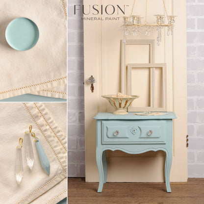 A light blue cabinet, decorative earrings, and small bowl painted in Inglenook from Fusion Mineral Paint range against a textured wall