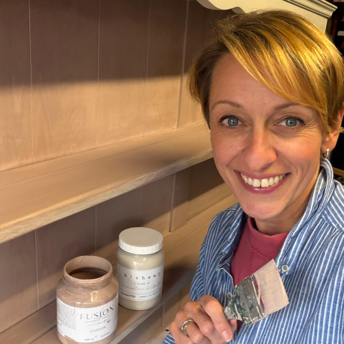 Jodi Walker of Upcycled & Reloved by Jodi stands in front of a piece of furniture with Fusion Mineral Paint and a paint brush in her hand offering classes in upcycling in Surrey