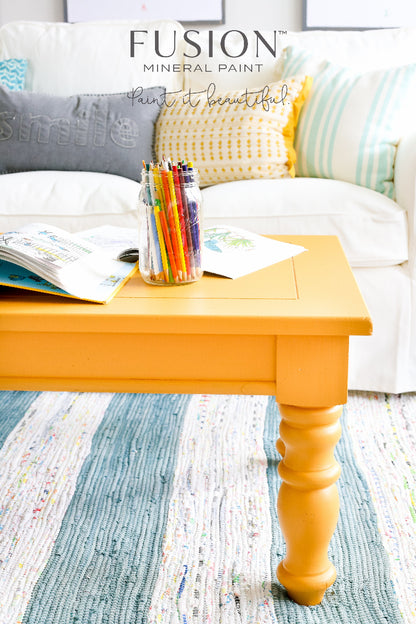 Mustard painted coffee table with colourful pencils and books in front of a white couch