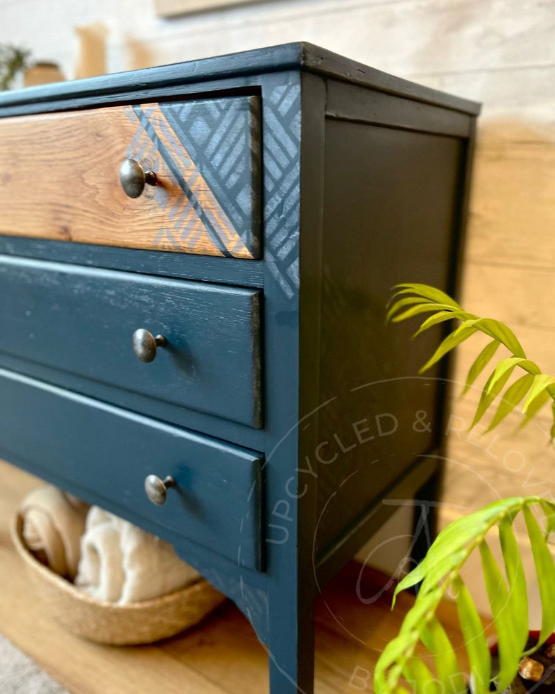 Exposed wood grain top drawer with silver geometric stencil detail on a refinished chest of drawers painted in Fusion Mineral Paint Willowbank, a rich navy blue.