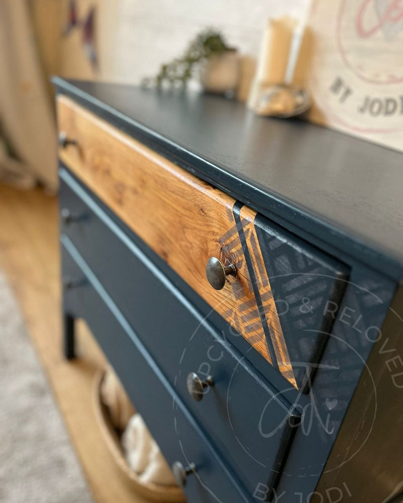 Exposed wood grain top drawer with silver geometric stencil detail on a refinished chest of drawers painted in Fusion Mineral Paint Willowbank, a rich navy blue.